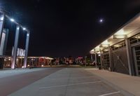 an empty parking lot at night with lights on the building's side and a parking area at the end