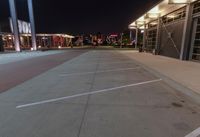 an empty parking lot at night with lights on the building's side and a parking area at the end