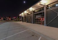 an empty parking lot at night with lights on the building's side and a parking area at the end