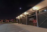 an empty parking lot at night with lights on the building's side and a parking area at the end