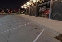 an empty parking lot at night with lights on the building's side and a parking area at the end