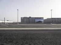 cars parked in an empty lot with an outside billboard on a building in the back ground