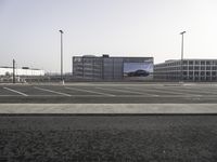 cars parked in an empty lot with an outside billboard on a building in the back ground