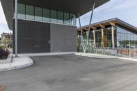 an empty parking lot at a city building near trees and bushes in the foreground