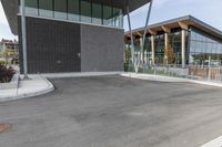 an empty parking lot at a city building near trees and bushes in the foreground