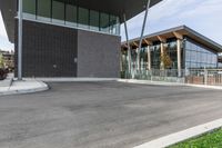 an empty parking lot at a city building near trees and bushes in the foreground