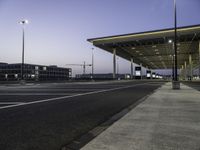 empty parking lot with lights on the side of it at dusk with buildings and a car parked nearby