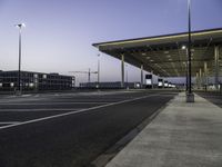 empty parking lot with lights on the side of it at dusk with buildings and a car parked nearby