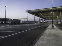 empty parking lot with lights on the side of it at dusk with buildings and a car parked nearby