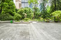 an empty parking lot filled with plants and trees in a city setting in front of a tall glass building