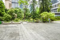 an empty parking lot filled with plants and trees in a city setting in front of a tall glass building