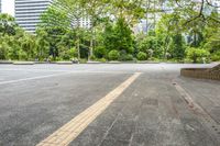 an empty parking lot filled with plants and trees in a city setting in front of a tall glass building