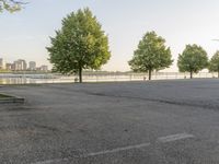 an empty parking lot with trees in the background and large cityscape in the distance