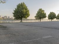 an empty parking lot with trees in the background and large cityscape in the distance