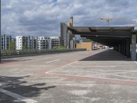 an empty parking lot with buildings and a road near by it on a partly cloudy day