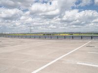 an empty parking lot with a field of green grass and flowers behind the space are blue skies