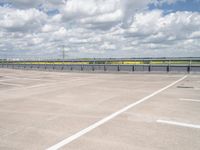 an empty parking lot with a field of green grass and flowers behind the space are blue skies