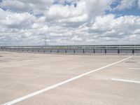 an empty parking lot with a field of green grass and flowers behind the space are blue skies