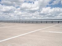 an empty parking lot with a field of green grass and flowers behind the space are blue skies