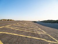 an empty parking lot with no people around it near some sand dunes at the beach