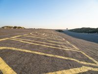 an empty parking lot with no people around it near some sand dunes at the beach