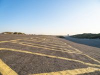 an empty parking lot with no people around it near some sand dunes at the beach