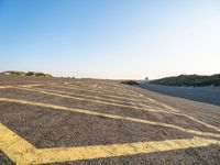 an empty parking lot with no people around it near some sand dunes at the beach