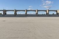 an empty parking lot with concrete bridge on the side of it in front of a cloud filled sky