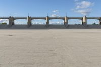 an empty parking lot with concrete bridge on the side of it in front of a cloud filled sky