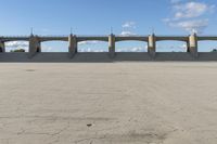 an empty parking lot with concrete bridge on the side of it in front of a cloud filled sky