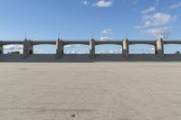 an empty parking lot with concrete bridge on the side of it in front of a cloud filled sky