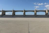 an empty parking lot with concrete bridge on the side of it in front of a cloud filled sky