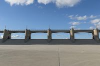 an empty parking lot with concrete bridge on the side of it in front of a cloud filled sky