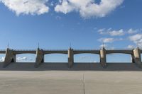 an empty parking lot with concrete bridge on the side of it in front of a cloud filled sky