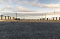 a paved parking lot that has been empty with a fence on one side and lighting poles around the perimeter