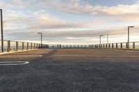 a paved parking lot that has been empty with a fence on one side and lighting poles around the perimeter