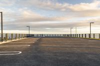 a paved parking lot that has been empty with a fence on one side and lighting poles around the perimeter