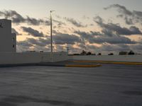 this parking lot is empty but the sky is very cloudy as the sun sets over it