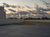 this parking lot is empty but the sky is very cloudy as the sun sets over it