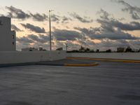 this parking lot is empty but the sky is very cloudy as the sun sets over it