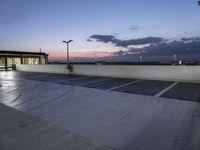 the empty parking lot has lights and an illuminated building at the background at dusk in the foreground is clouds