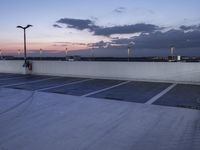 the empty parking lot has lights and an illuminated building at the background at dusk in the foreground is clouds