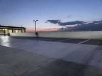 the empty parking lot has lights and an illuminated building at the background at dusk in the foreground is clouds