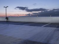 the empty parking lot has lights and an illuminated building at the background at dusk in the foreground is clouds