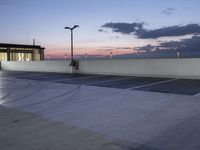 the empty parking lot has lights and an illuminated building at the background at dusk in the foreground is clouds