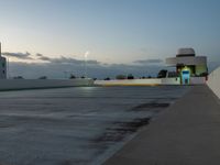 an empty parking lot at dusk with sky in background and a building behind it, under a cloudy blue sky