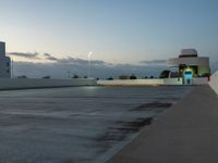 an empty parking lot at dusk with sky in background and a building behind it, under a cloudy blue sky