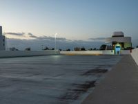 an empty parking lot at dusk with sky in background and a building behind it, under a cloudy blue sky