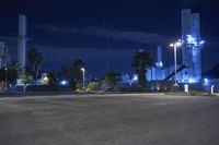 an empty parking lot next to a factory at night, lit up by street lights