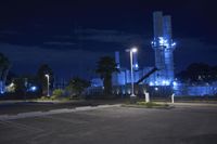 an empty parking lot next to a factory at night, lit up by street lights